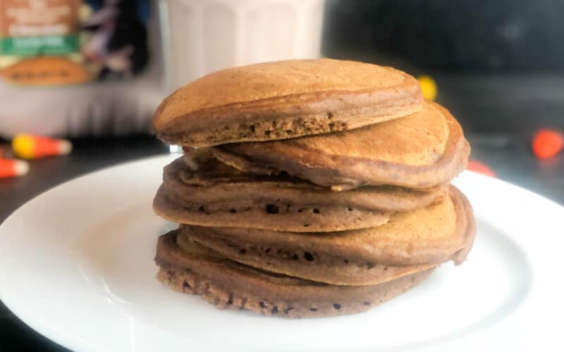 stack of chocolate pumpkin pancakes with syrup and whipped cream