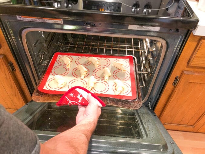 man's hand putting baked goods on a pan into the oven