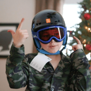 child with snowboard helmet on in front of xmas tree