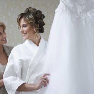 Bride in bathrobe touching wedding dress mother looking on