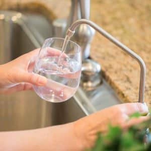 Woman Pouring Fresh Reverse Osmosis Purified Water Into Glass in Kitchen
