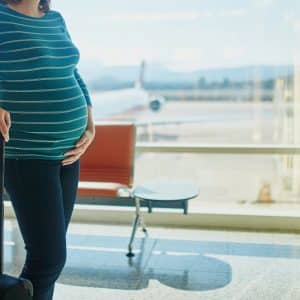 pregnant woman standing in airport with her hand on her belly