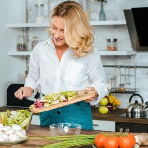 Beautiful adult woman making healthy salad at kitchen