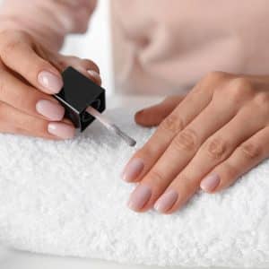 Woman applying nail polish at table, closeup. At-home manicure