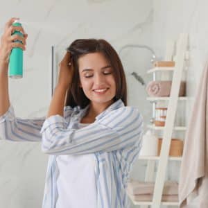 Woman applying dry shampoo onto her hair in bathroom