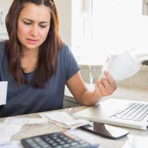 Young woman getting stressed over finances in front of laptop in kitchen