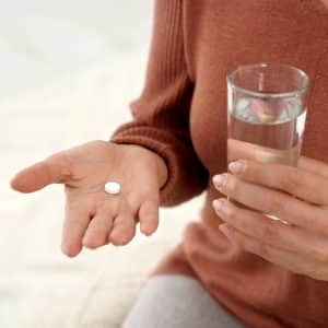 Woman's hands, one holding a pill and the other holding a glass of water.