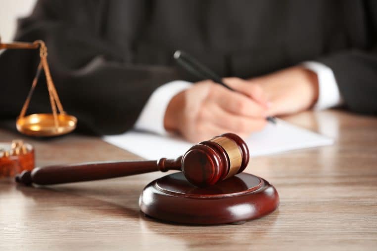 Judge writing on paper with gavel on wooden table indoors