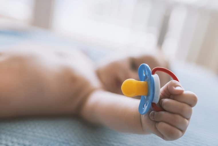 a baby's hand holding a pacifier in a crib