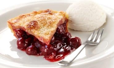 a slice of cherry pie on a white plate with a scoop of vanilla ice cream and a fork