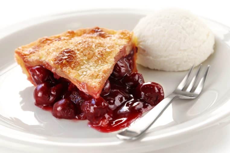 a slice of cherry pie on a white plate with a scoop of vanilla ice cream and a fork
