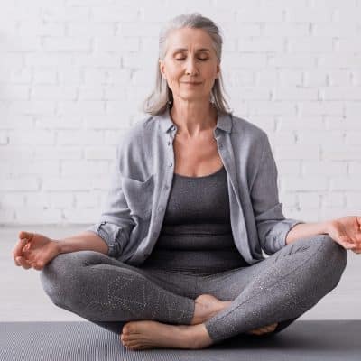 gray haired woman meditating on a yoga mat
