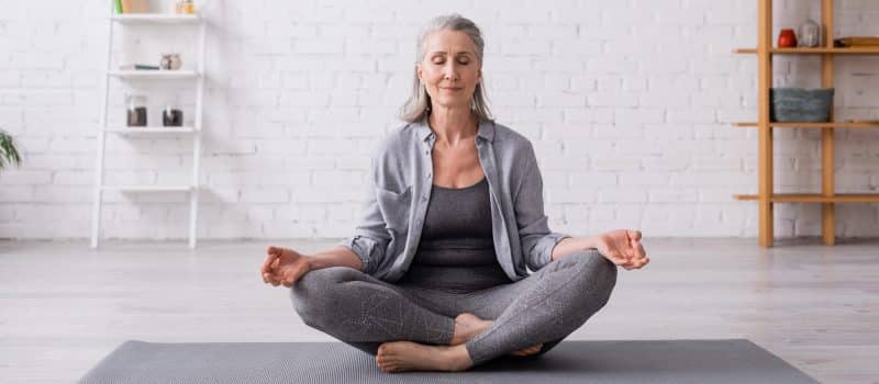 gray haired woman meditating on a yoga mat