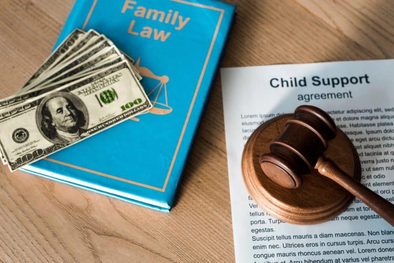 Wooden gavel near document with child support agreement, dollar banknotes and family law