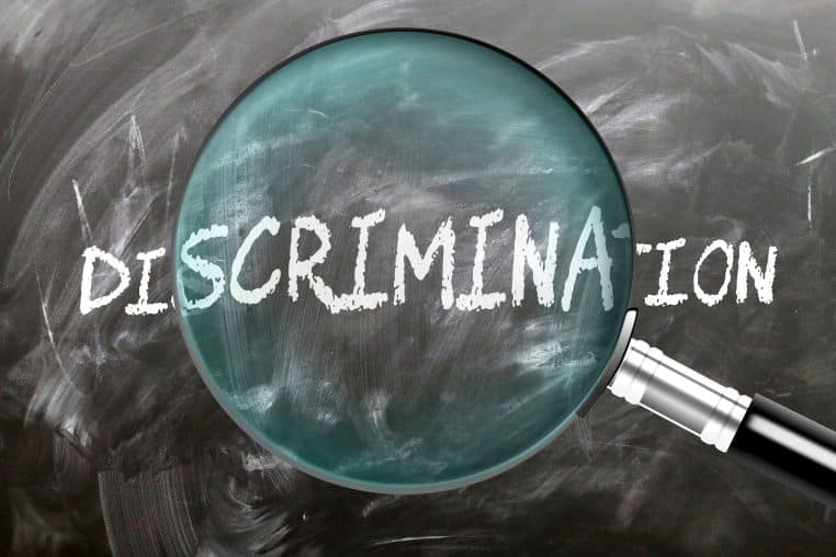 A magnifying glass enlarging word 'discrimination' written on a blackboard