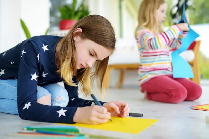 Two young sisters drawing with colorful pencils at home. Creative kids doing crafts together. Education and distance learning for kids. Homeschooling during quarantine. Stay at home entertainment.