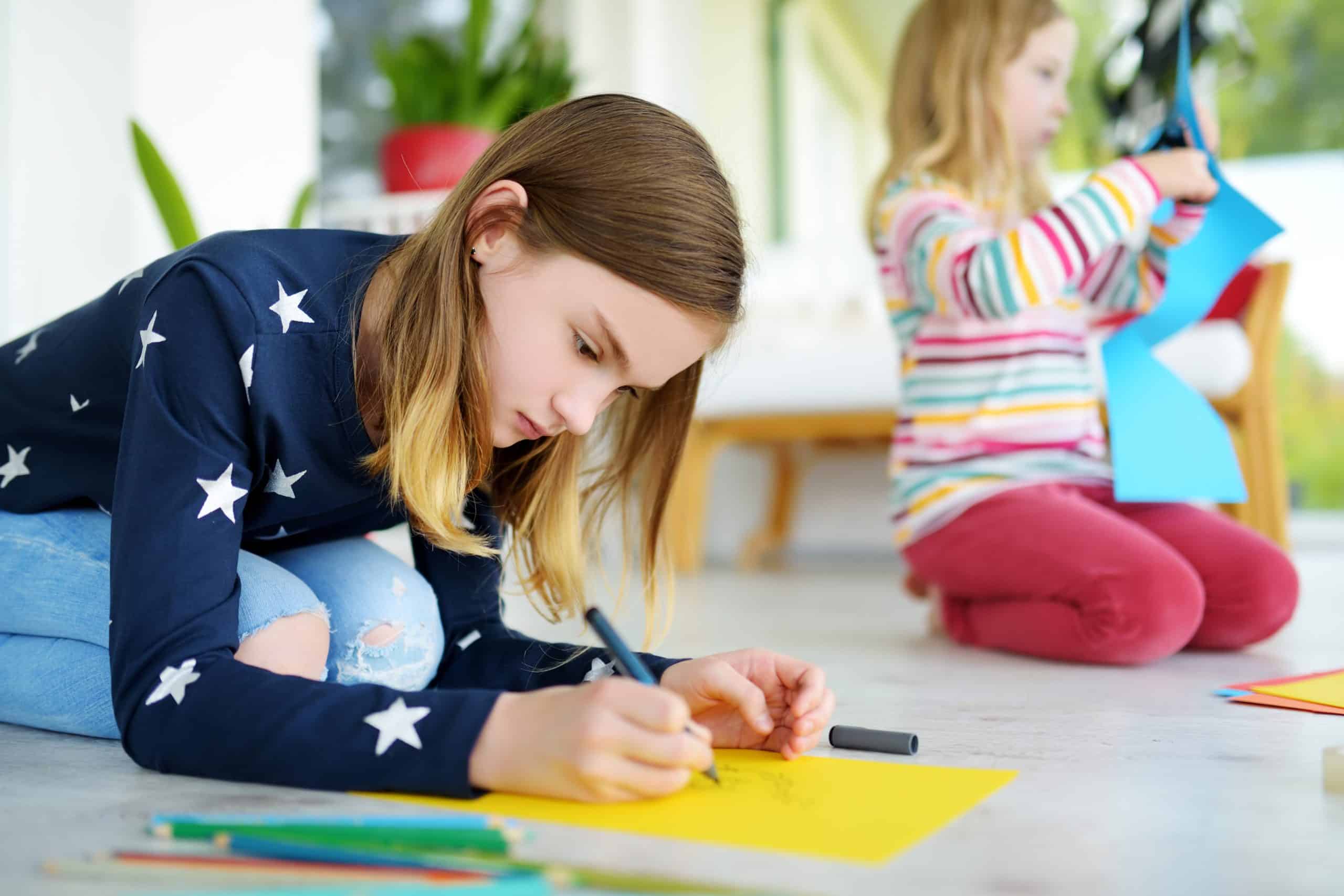 Two young sisters drawing with colorful pencils at home. Creative kids doing crafts together. Education and distance learning for kids. Homeschooling during quarantine. Stay at home entertainment.