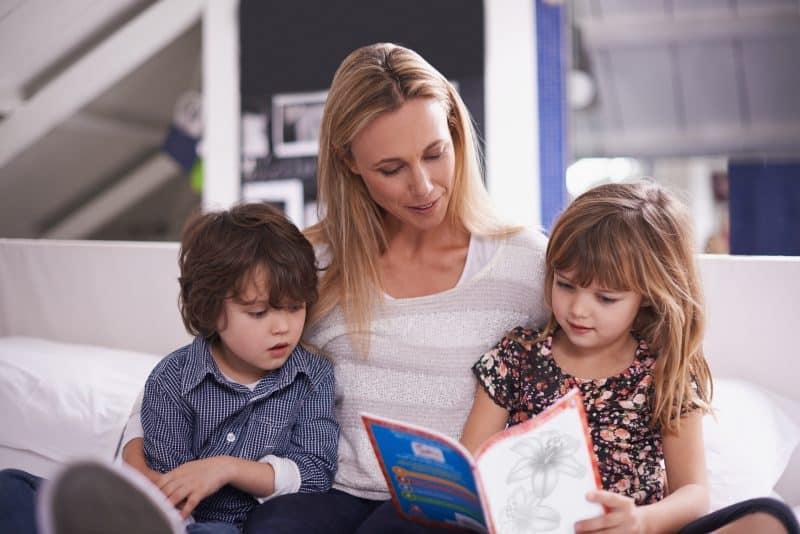 Reading, mother and children on couch with book for bonding, teaching and learning together in home. Woman, son and daughter relax on sofa with storytelling, smile and happy family in living room.