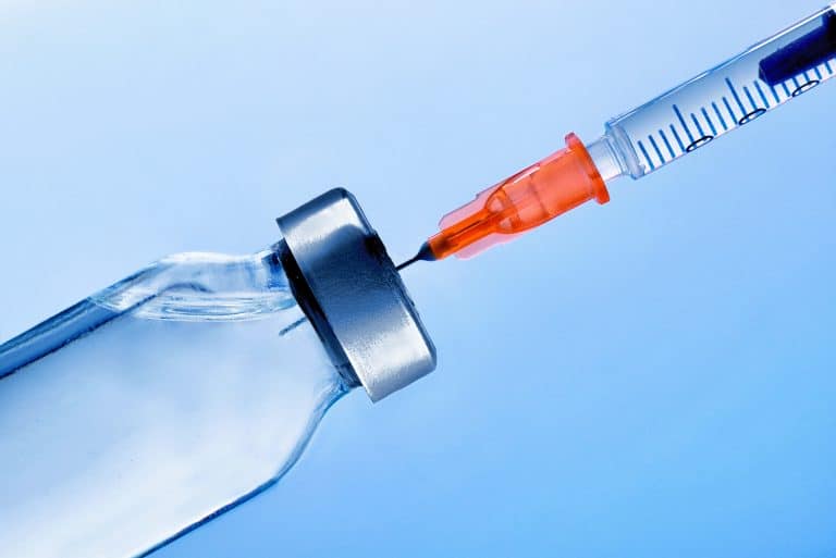 Vial with medication and punctured syringe close up with blue background. Horizontal composition. Front view.