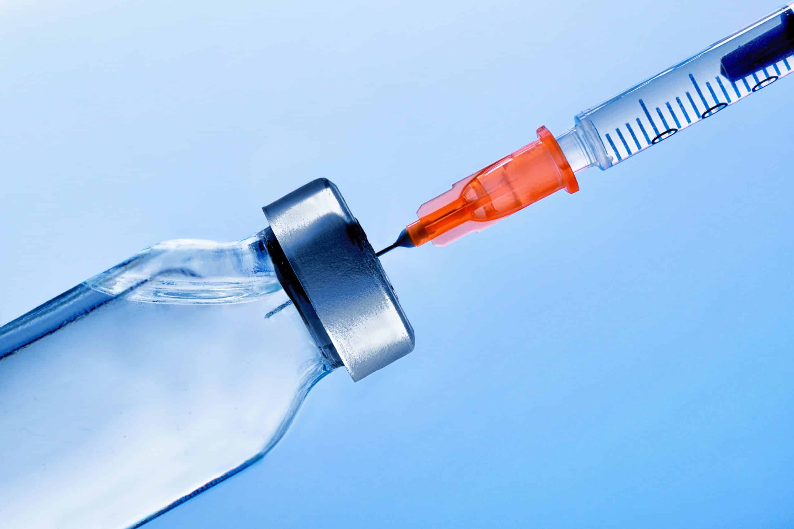 Vial with medication and punctured syringe close up with blue background. Horizontal composition. Front view.
