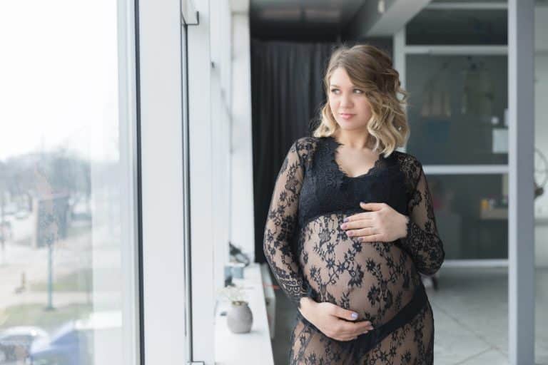 Pregnant woman in a beautiful lace dress holds belly