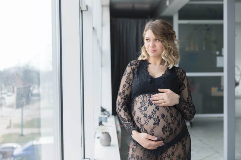 Pregnant woman in a beautiful lace dress holds belly