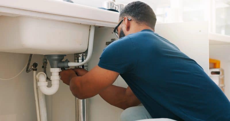 Plumber black man, kitchen and sink maintenance with tools, focus and pipe repair for drainage in home. Entrepreneur handyman, plumbing expert or small business owner in house for fixing water system. Plumber Black Man Kitchen Sink Maintenance Tools Focus Pipe Repair Drainage Home Entrepreneur Handyman Plumbing Expert Small Business Owner House Fixing Water System