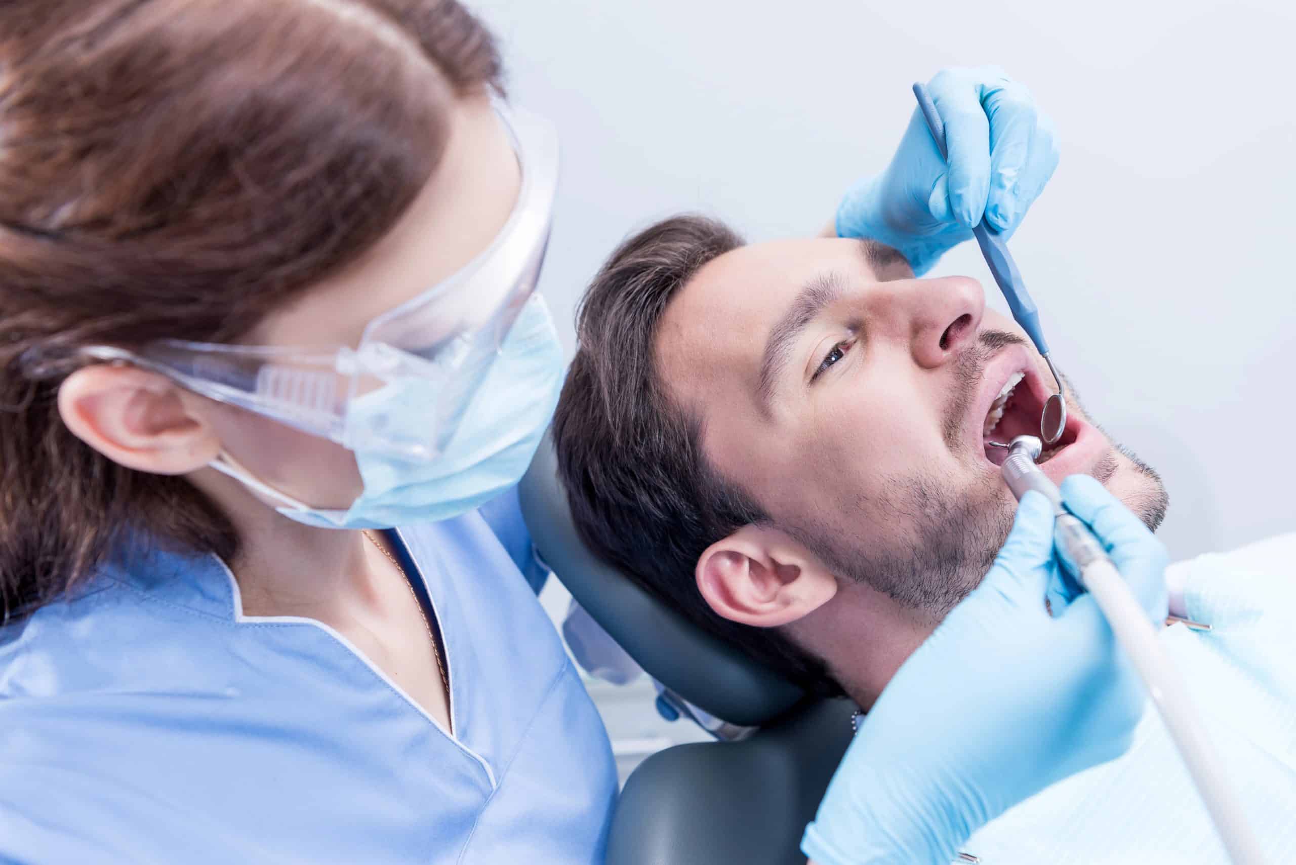 Dentist in protective mask and glasses curing teeth of patient Dentist curing patients teeth