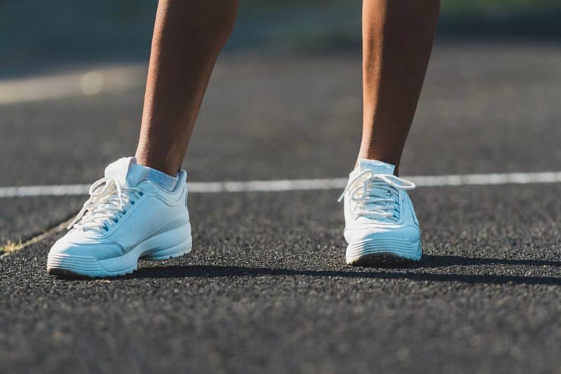 Womans legs in white running shoes standing on asphalt. Womans legs in white running shoes standing on asphalt