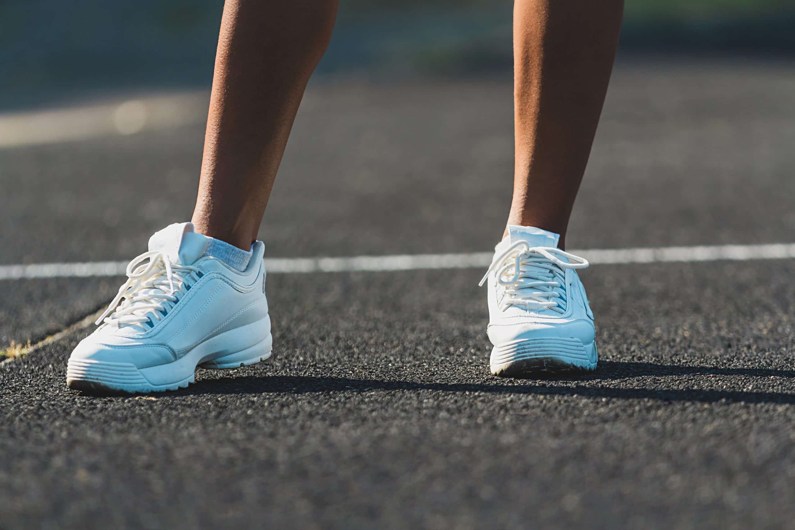 Womans legs in white running shoes standing on asphalt. Womans legs in white running shoes standing on asphalt
